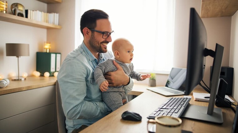 Sales Manager working from home holding his baby in front of the screen